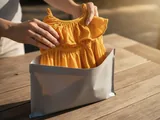Hands lifting a yellow summer dress out of a plain grey mailer bag
